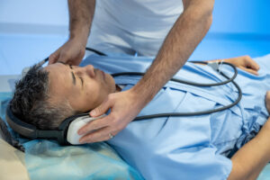 Male mixed race patient getting headphones before examination. Magnetic resonance imaging technology in specialized medical clinic.