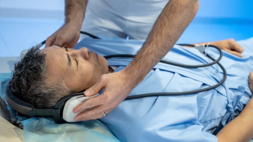 Male mixed race patient getting headphones before examination. Magnetic resonance imaging technology in specialized medical clinic.