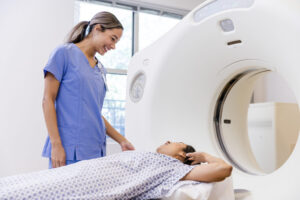 A mid adult woman talks to female radiographer before going through CT scan machine.
